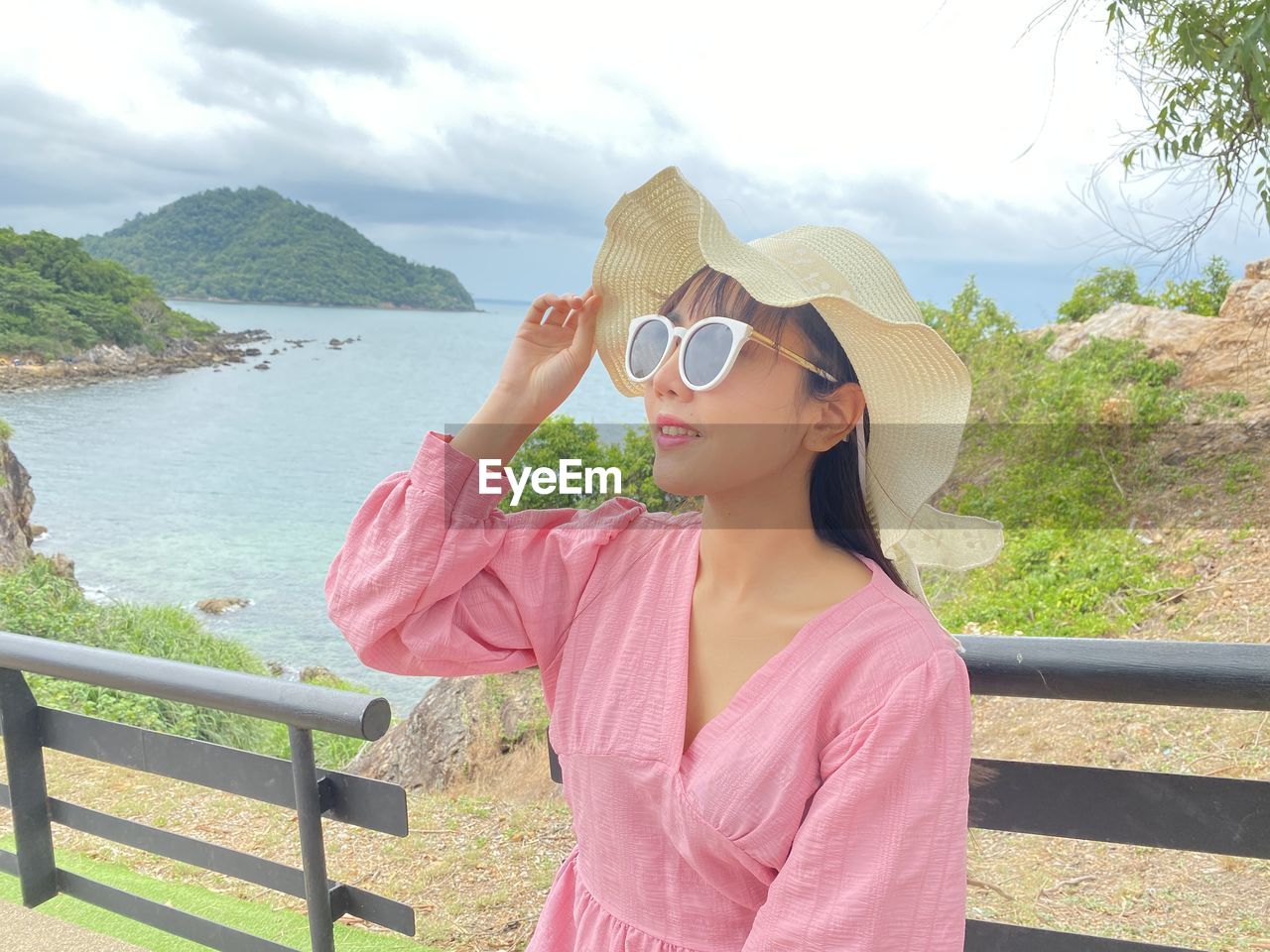 Woman wearing sunglasses standing by railing against water