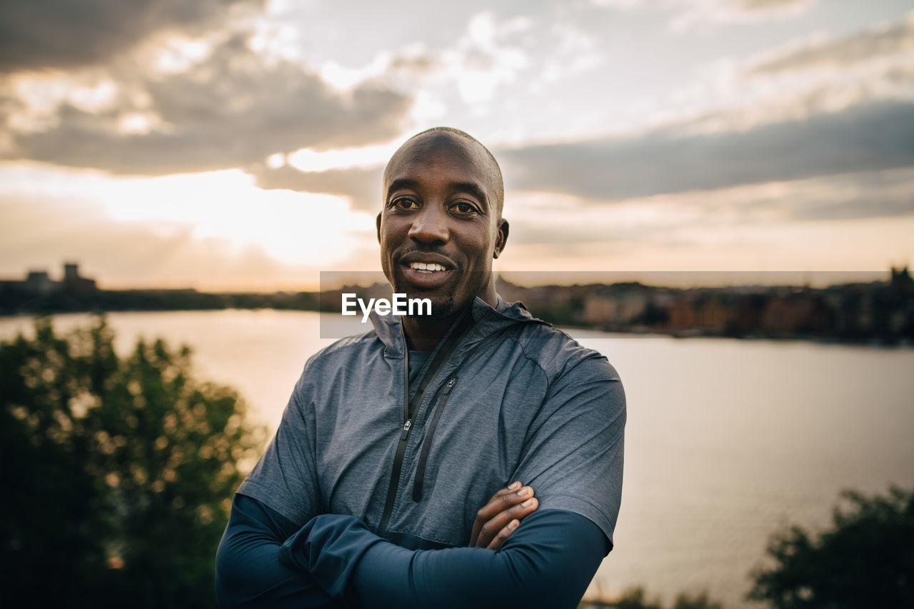 Portrait of confident male athlete standing on hill against sky during sunset