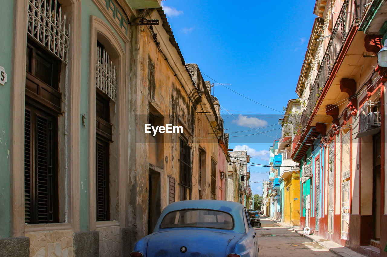 Old car on street amidst buildings against blue sky