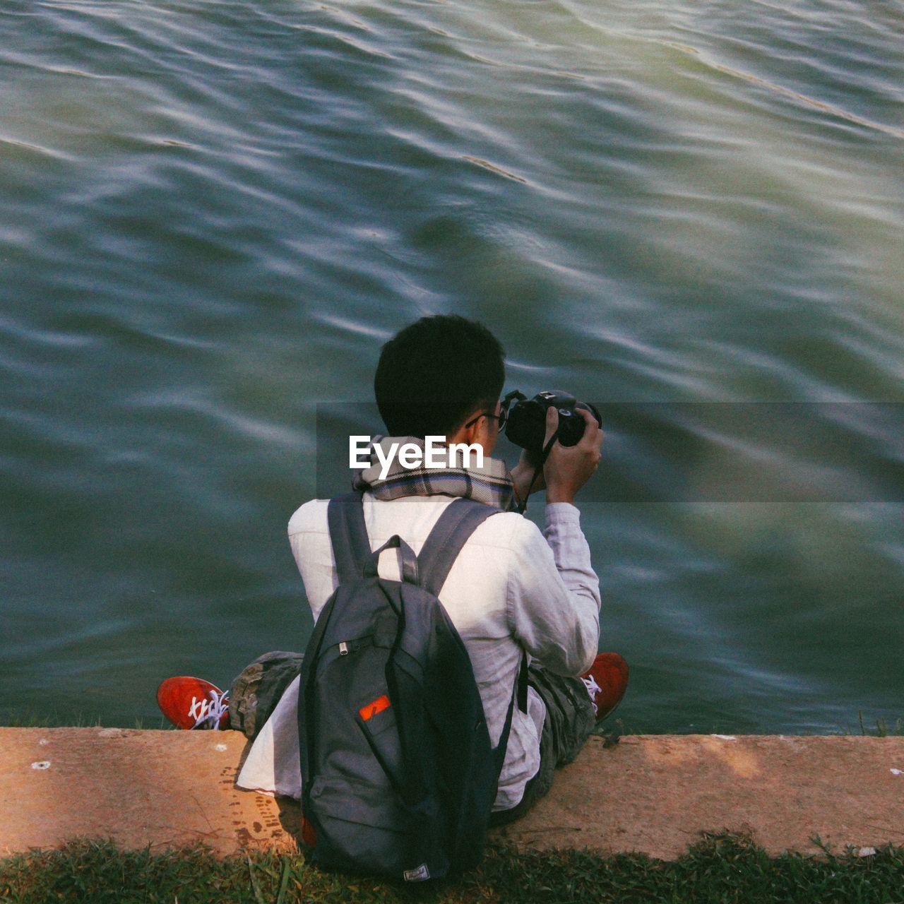 REAR VIEW OF MAN PHOTOGRAPHING WHILE SITTING ON WATER