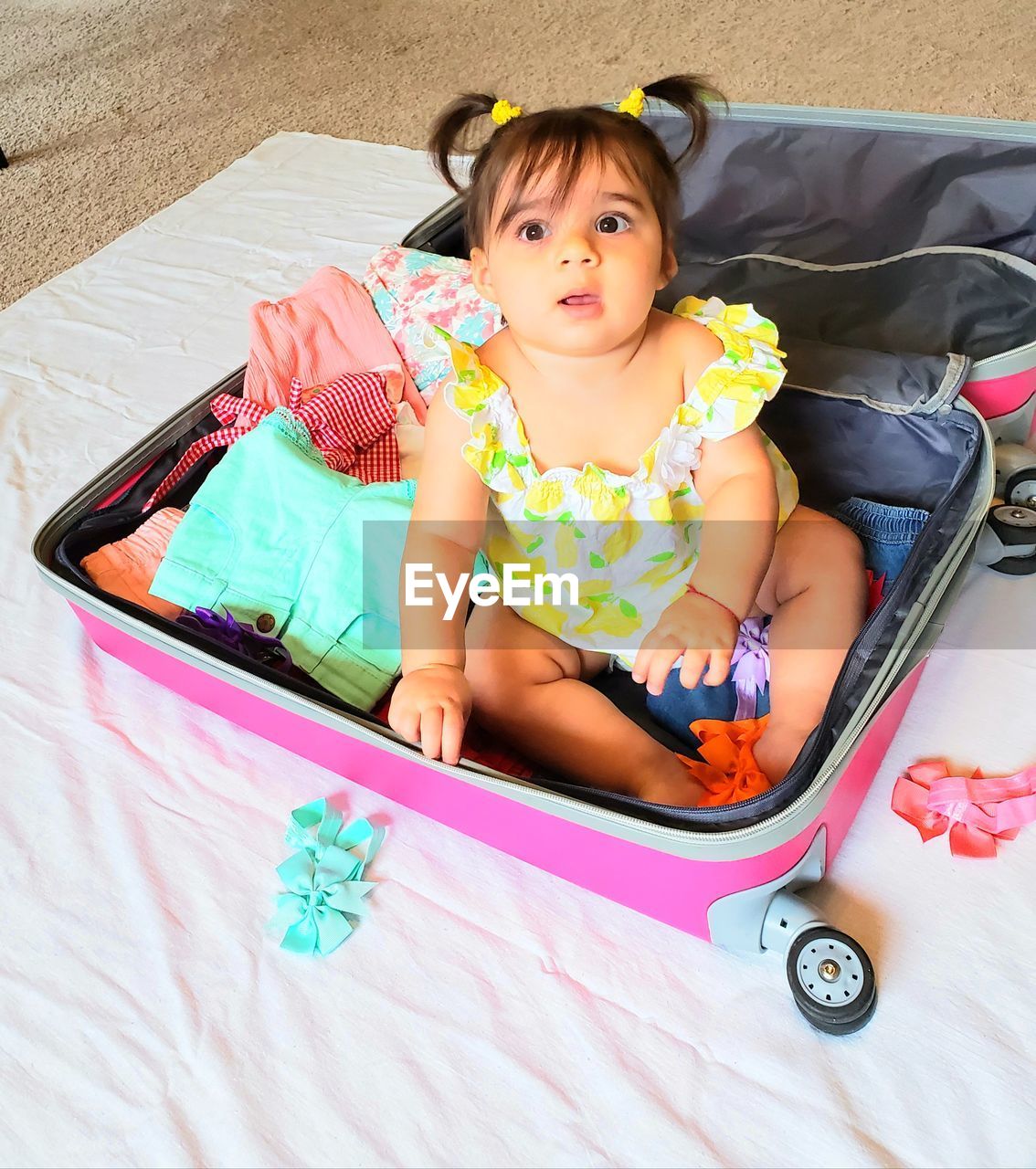 High angle view of cute baby girl sitting in suitcase on floor at home
