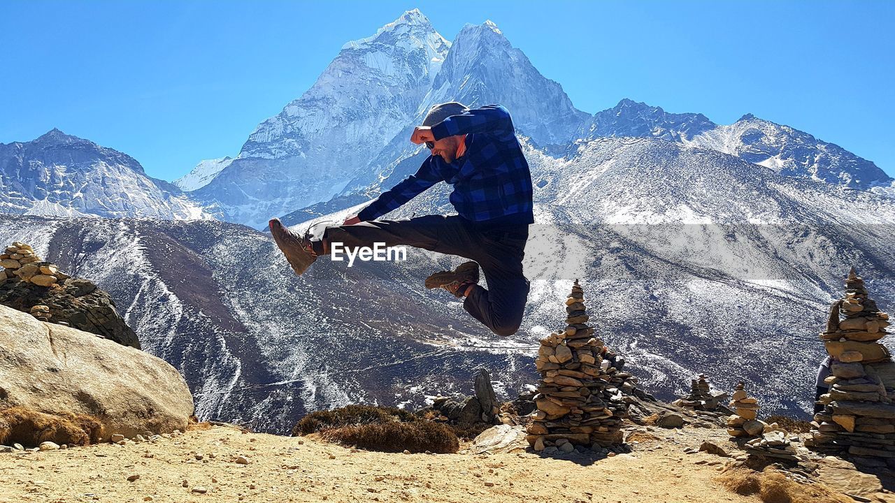 Full length of man jumping against snowcapped mountains