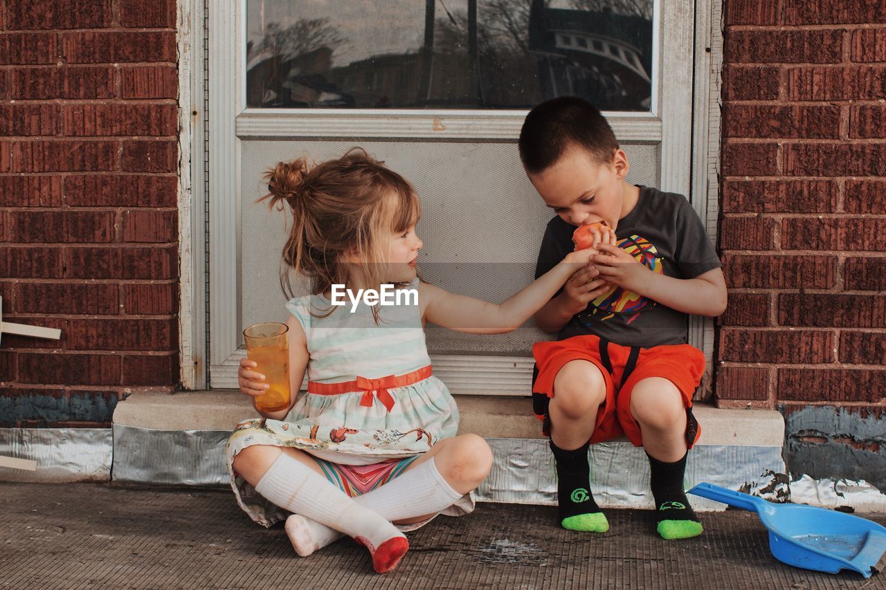 Siblings sitting on doorway against brick wall