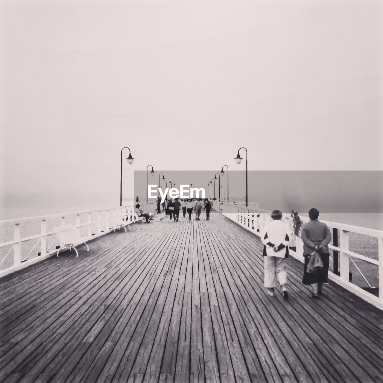 Rear view of people walking on jetty against clear sky