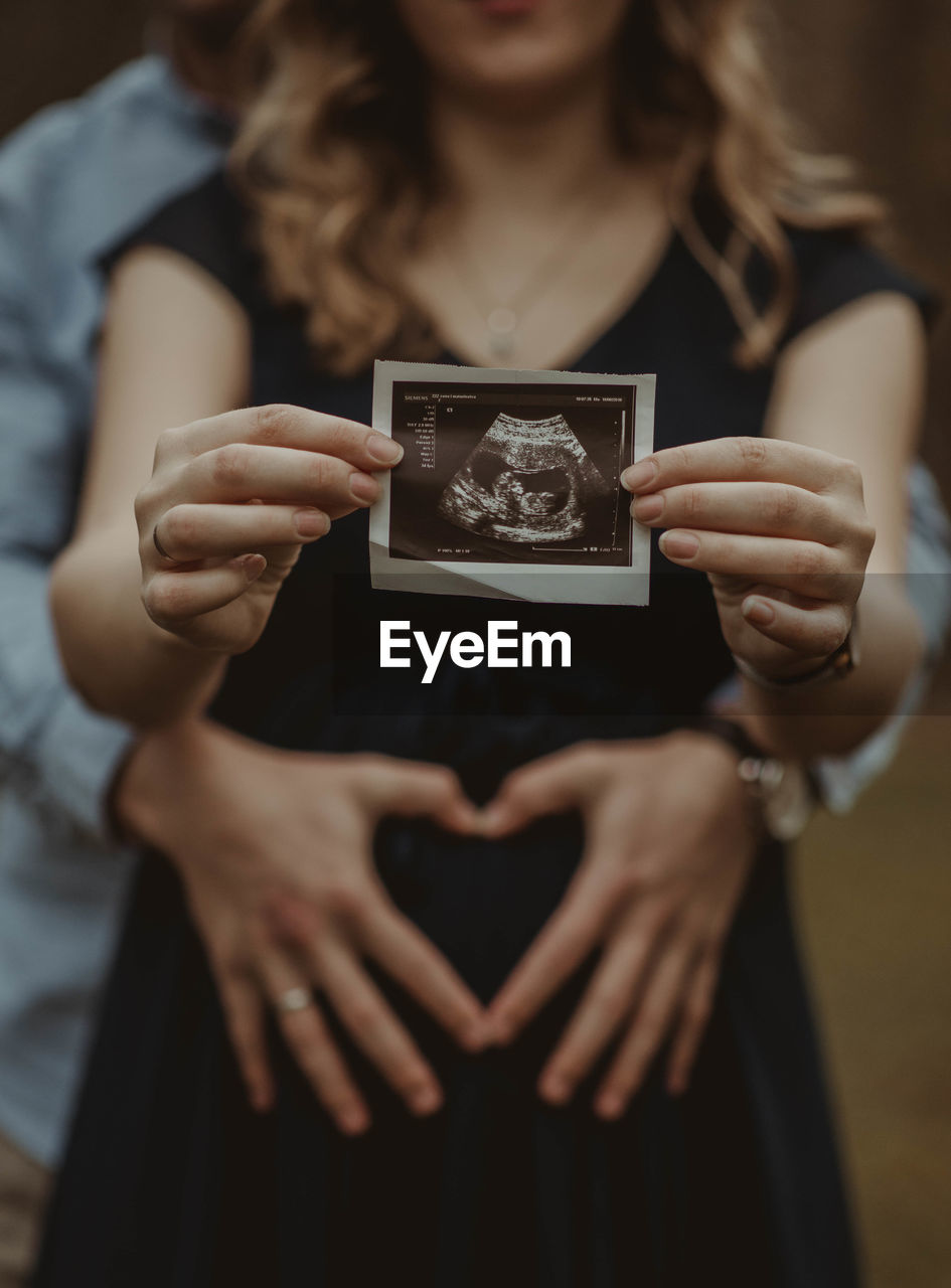 Midsection of pregnant woman holding ultrasound photo while standing with husband