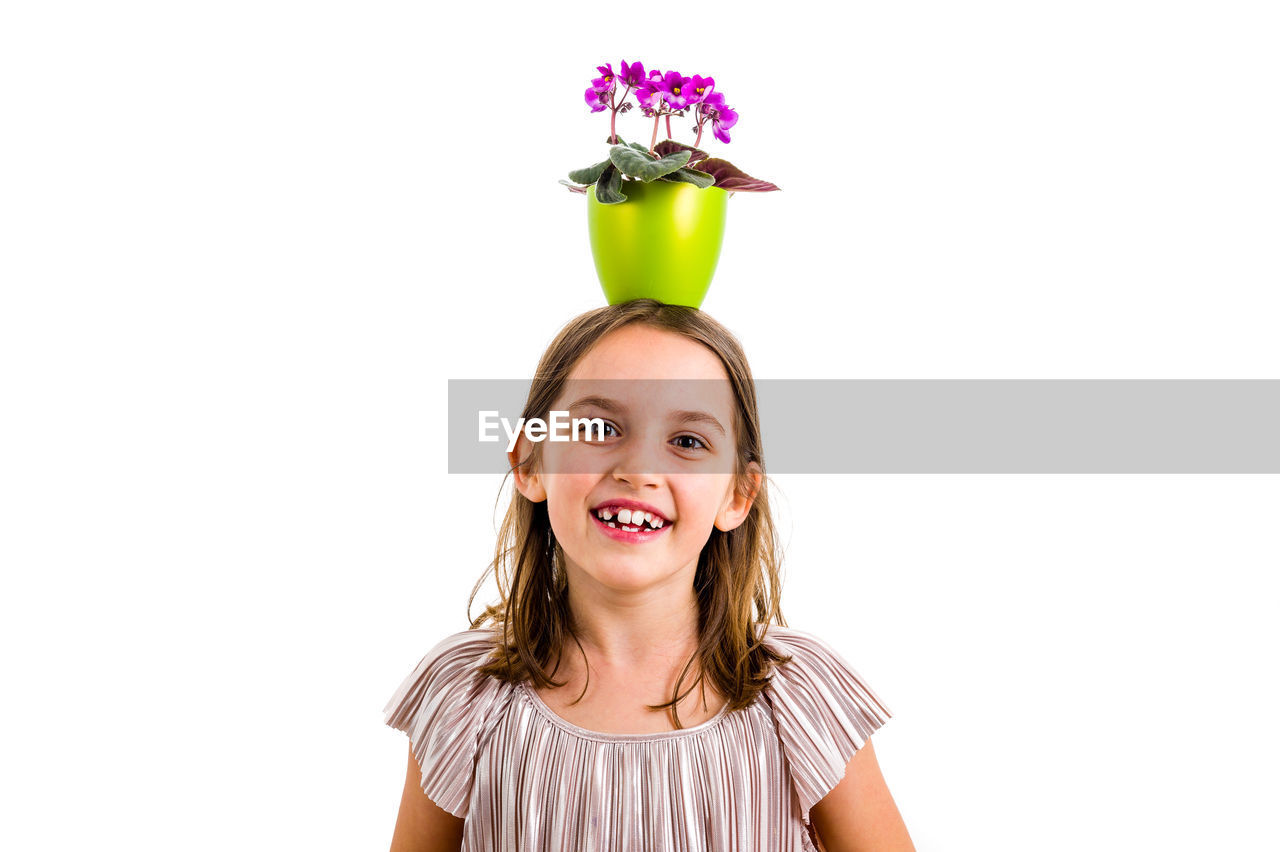 Portrait of girl with flower pot on head standing against white background