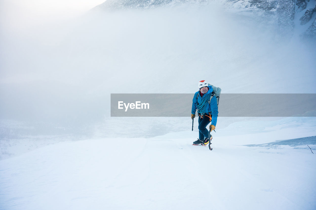 A male alpine climber ascends a steep section of snow with clouds