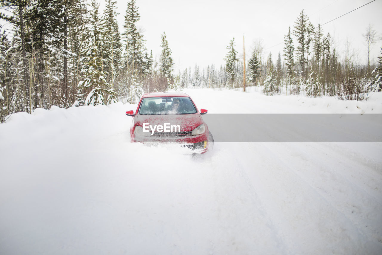 Front view of red car driving on snow covered road.
