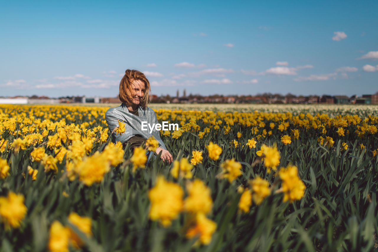 Girl sitting in a  yellow narcissus flowers field