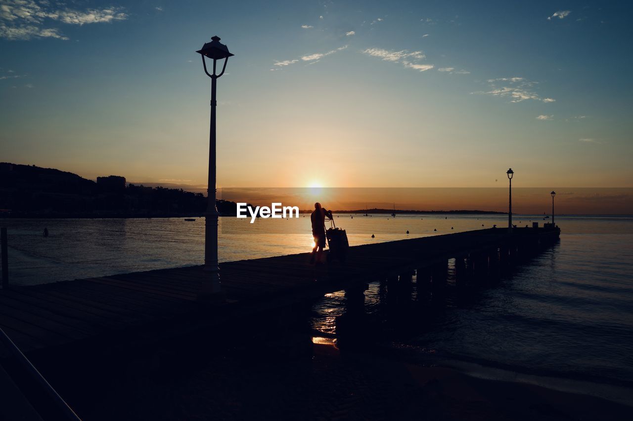 SILHOUETTE PERSON ON PIER OVER SEA AGAINST SKY DURING SUNSET