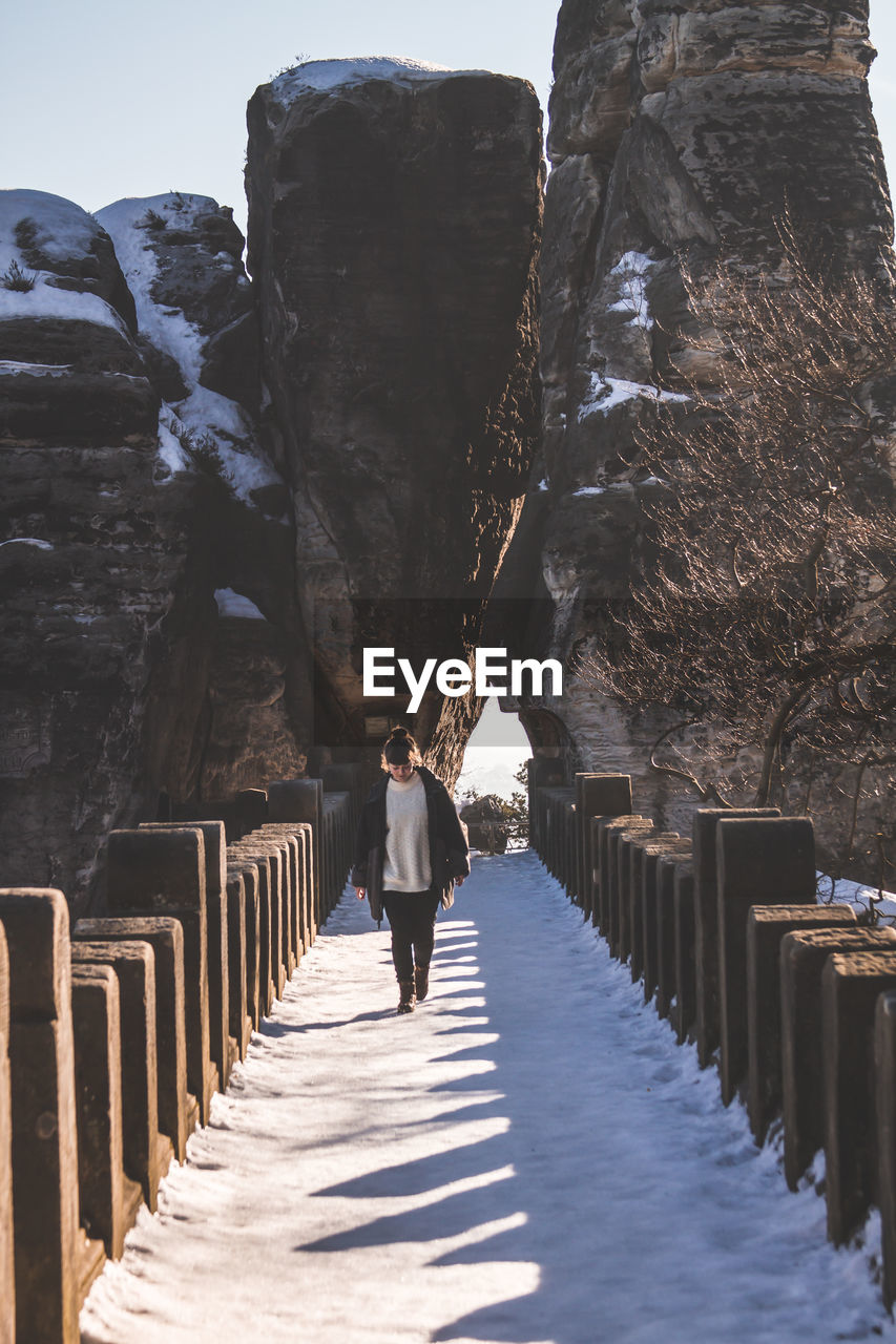 Woman walking on frozen footbridge against rock formations