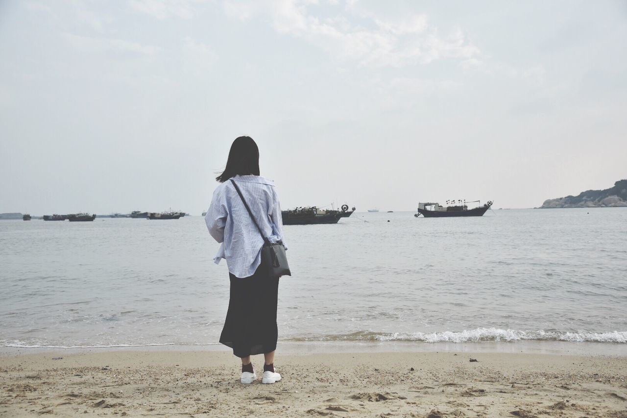 Rear view of woman standing on beach against sky