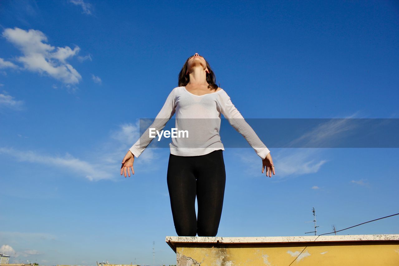 LOW ANGLE VIEW OF YOUNG WOMAN STANDING AGAINST SKY