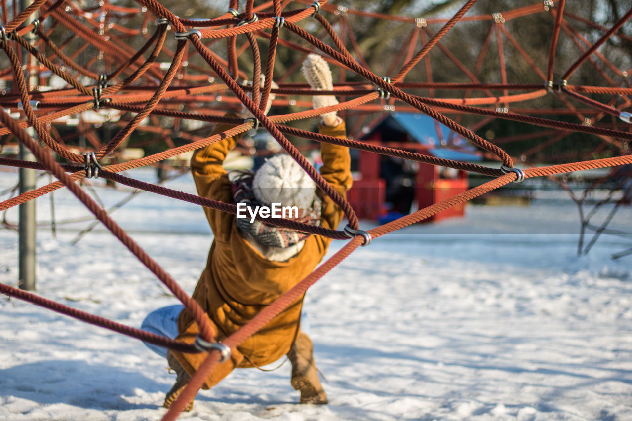 Full length rear view of woman climbing on ropes at snow covered park