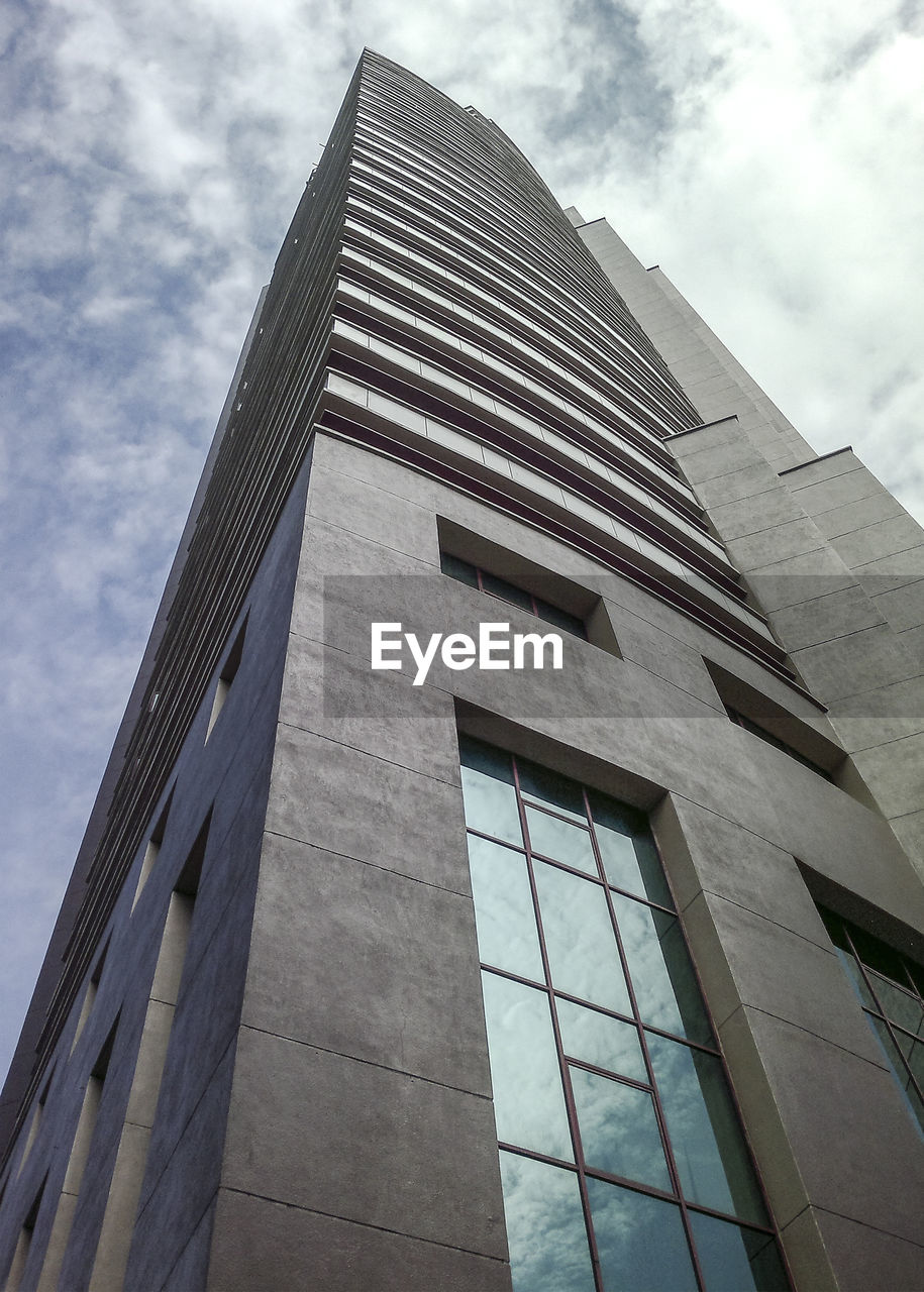 LOW ANGLE VIEW OF MODERN GLASS BUILDING AGAINST SKY