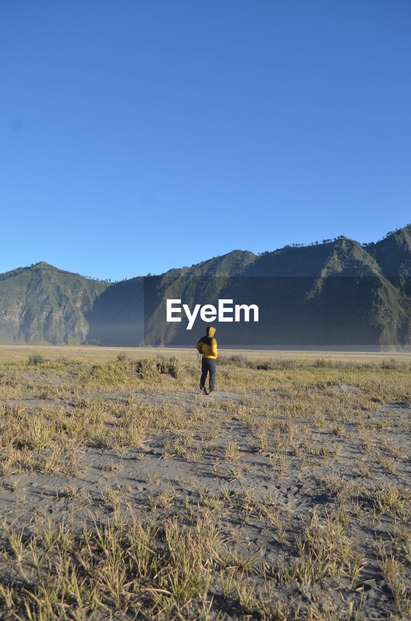 REAR VIEW OF MAN STANDING ON MOUNTAIN