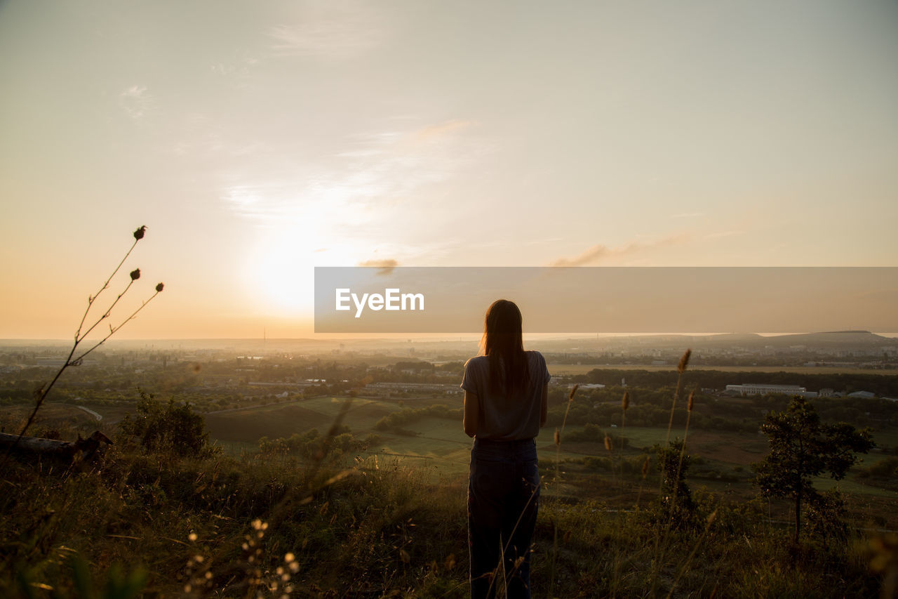 Rear view of woman looking at landscape against sky during sunset