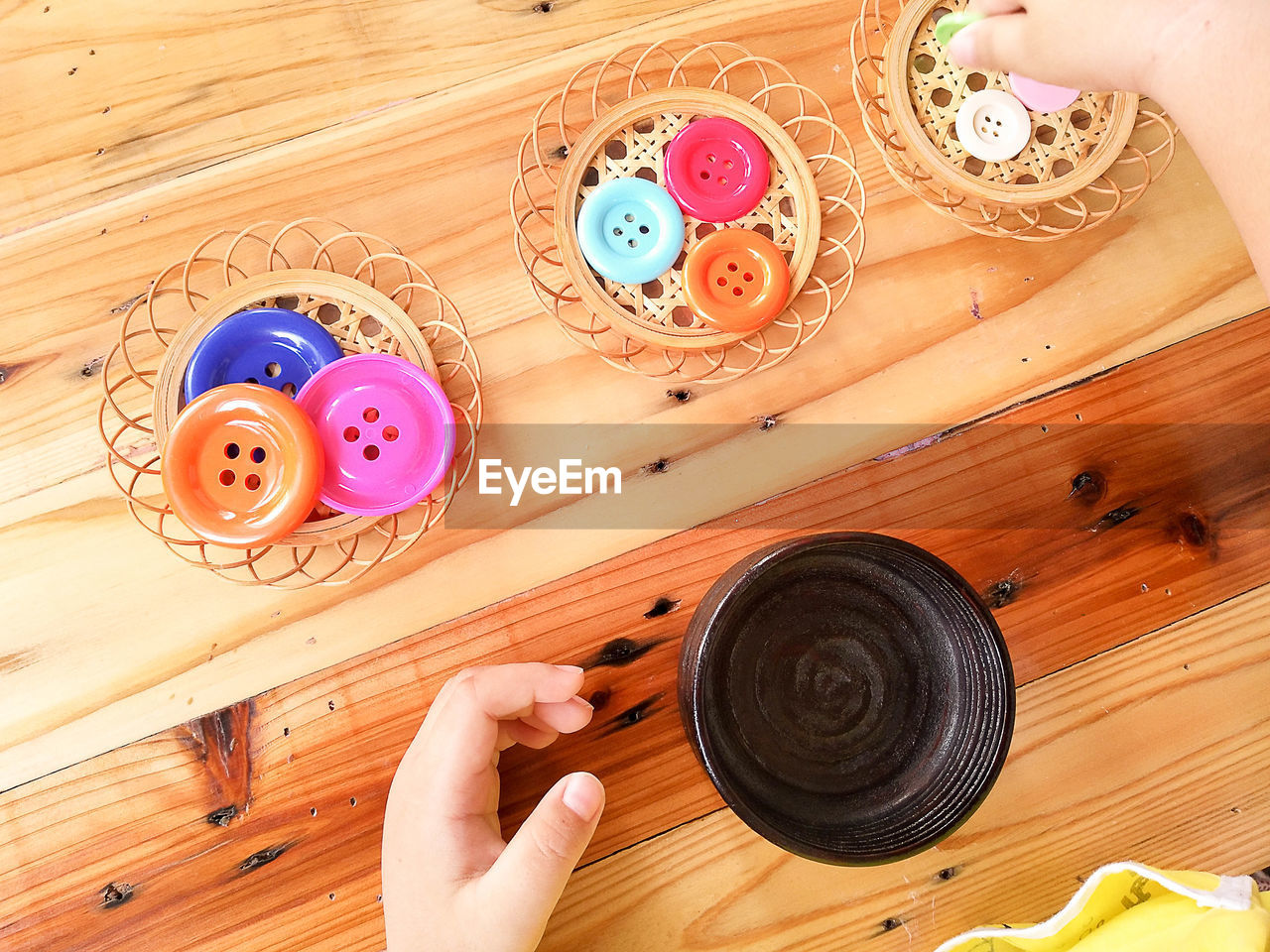 Cropped hand of child holding container by colorful buttons on wooden table