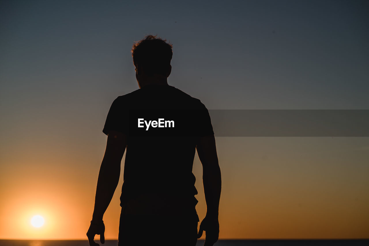 Silhouette man standing by sea against sky during sunset