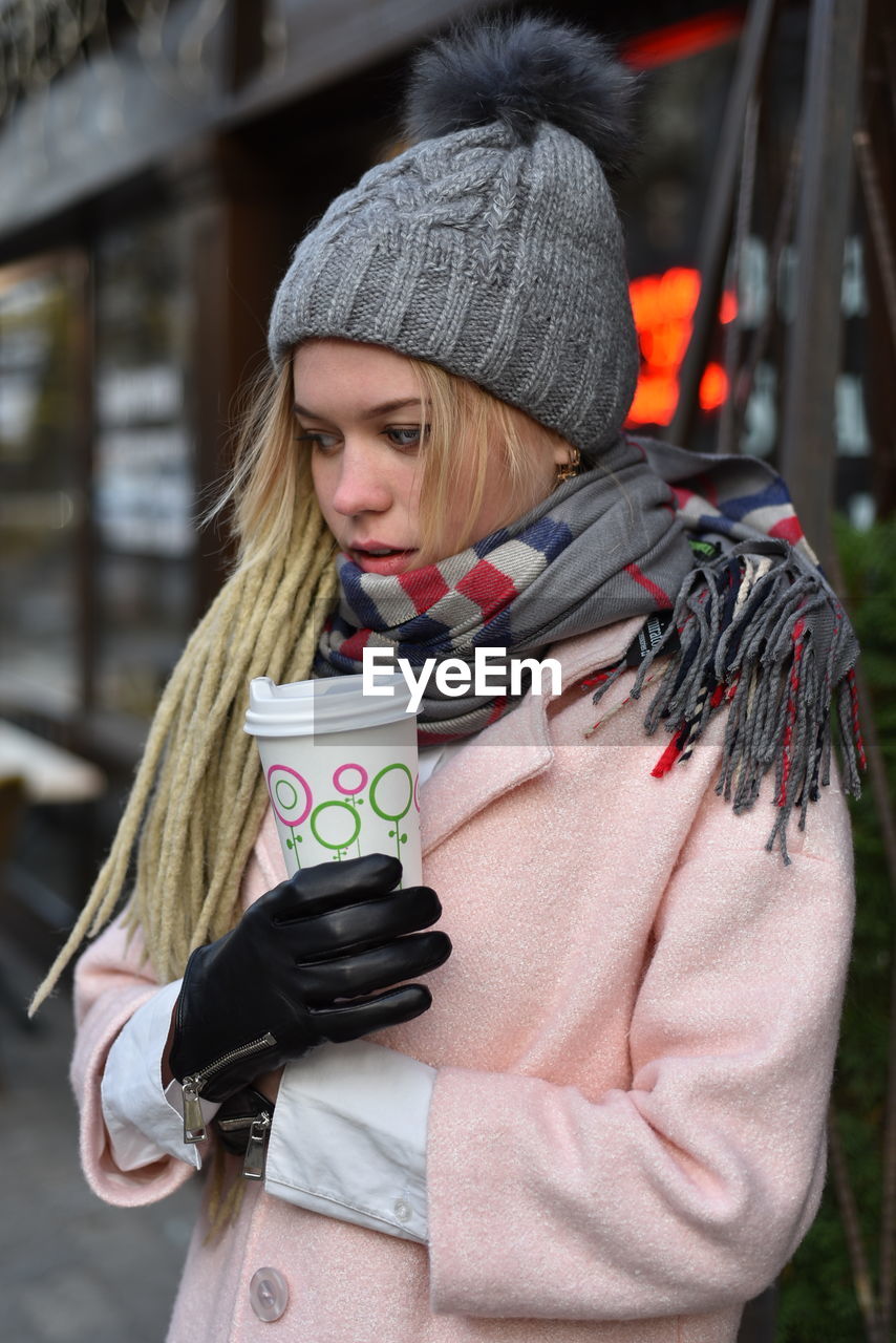 Young woman looking away while holding coffee cup in winter