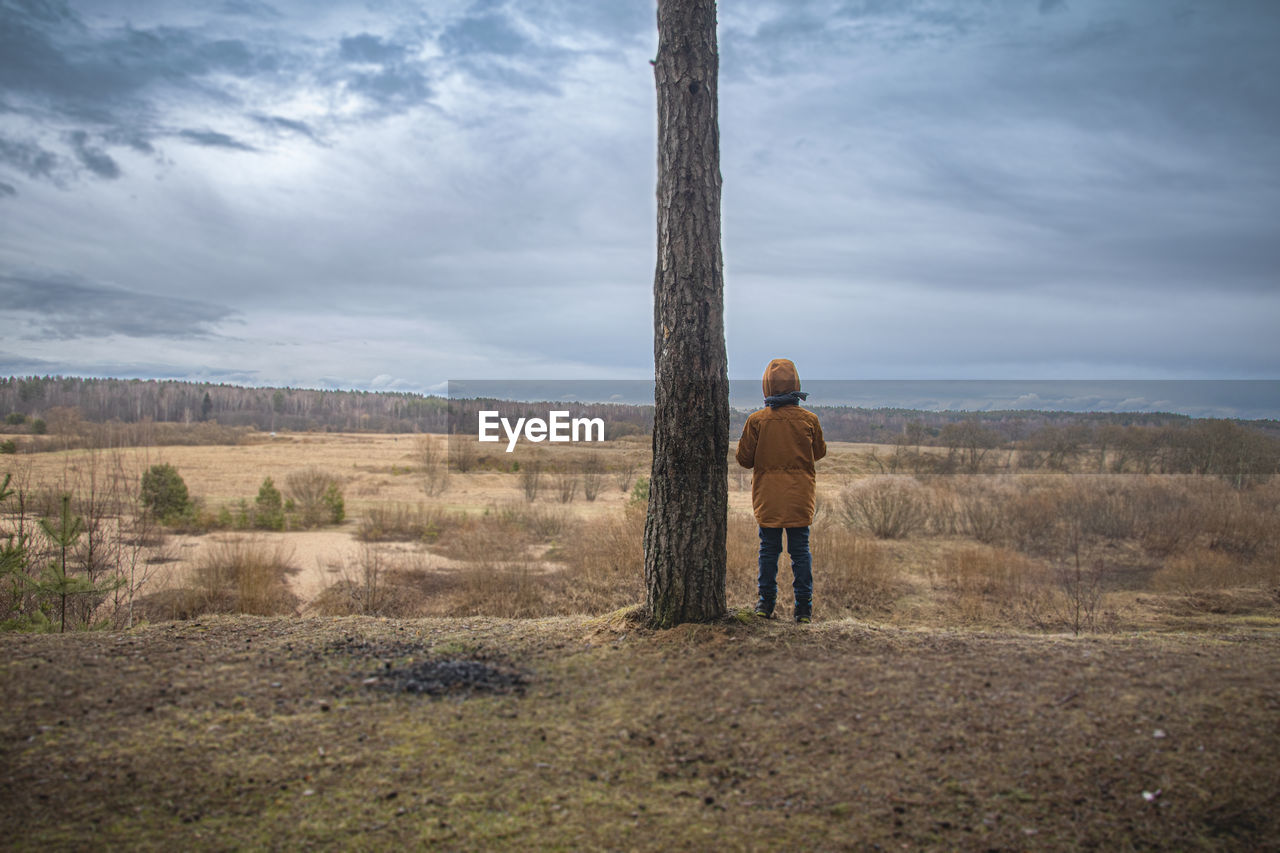 Rear view of child standing on field against sky