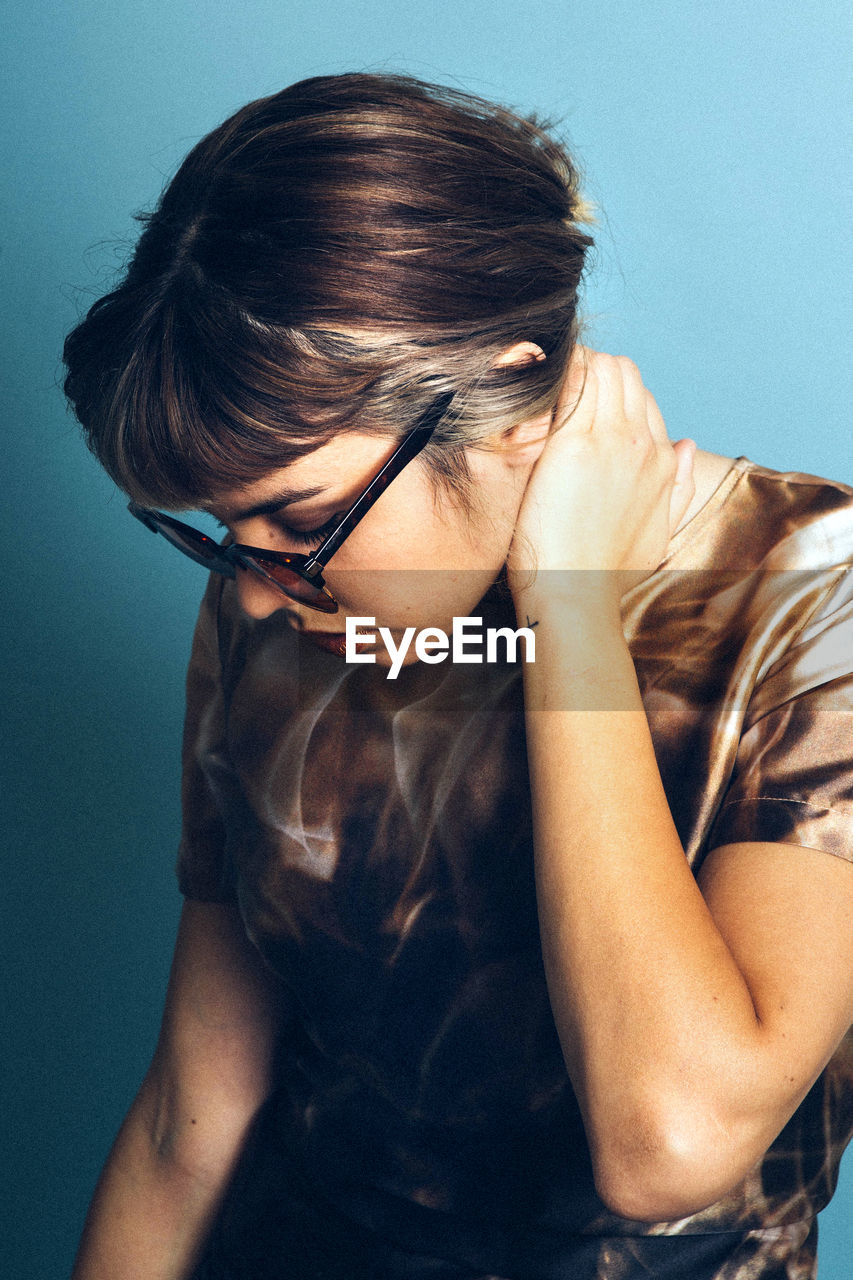 Close-up of young woman wearing sunglasses against blue background