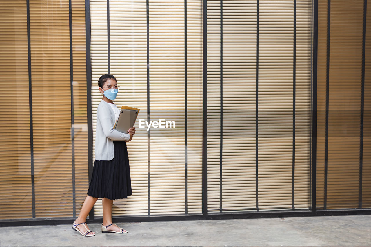 Full length of young woman standing against wall