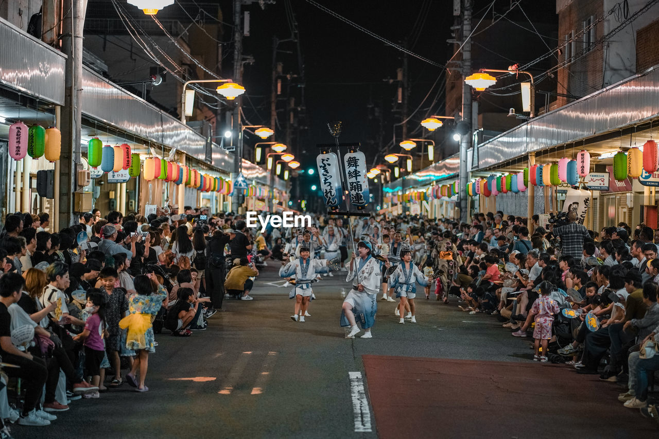 crowd, large group of people, street, road, city, architecture, group of people, building exterior, built structure, infrastructure, city life, urban area, city street, night, men, lifestyles, public space, adult, women, outdoors, downtown, market, transportation