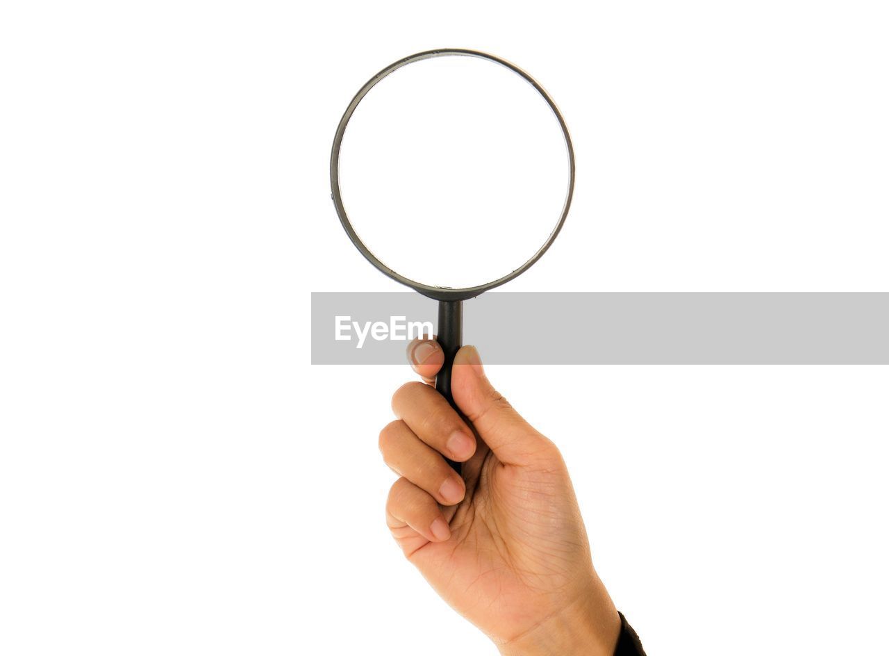 Cropped hand of woman holding magnifying glass against white background