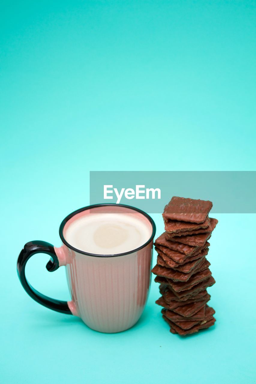 Pink mug of coffee and a stack of chocolate cookies on green background