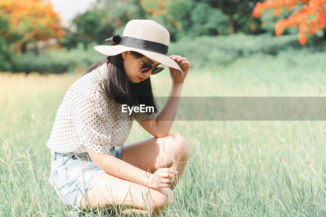 Young woman wearing hat crouching at park