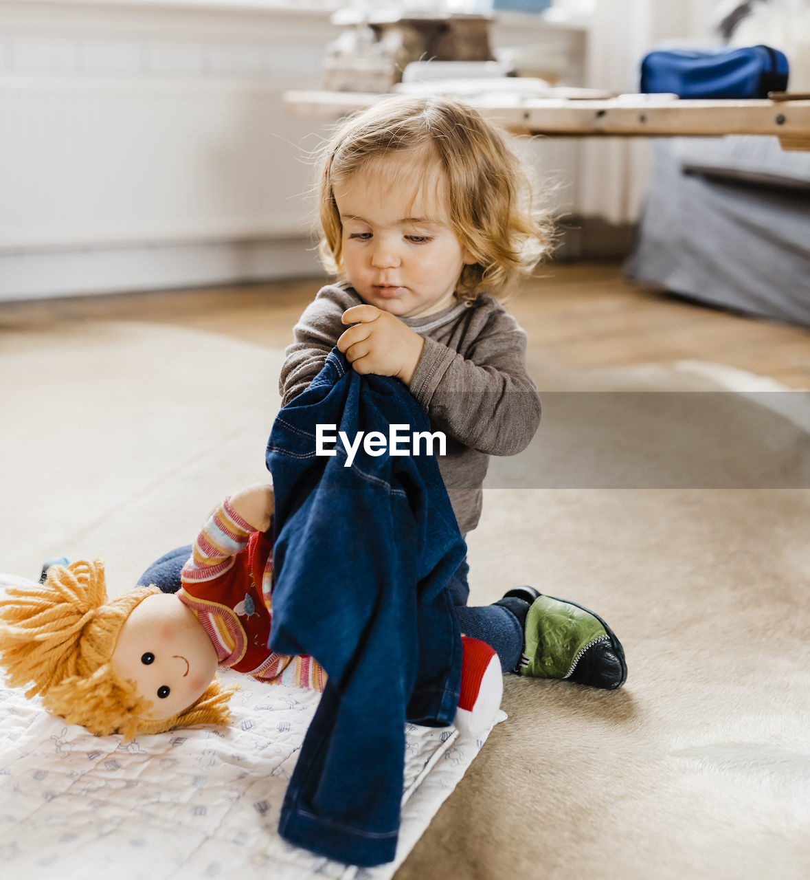 Cute child playing with doll on rug at home
