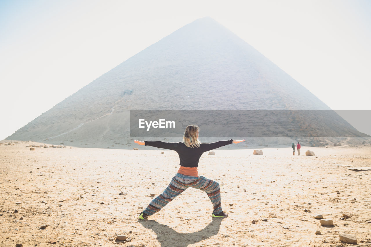 Full length of woman practicing yoga against pyramid at egypt