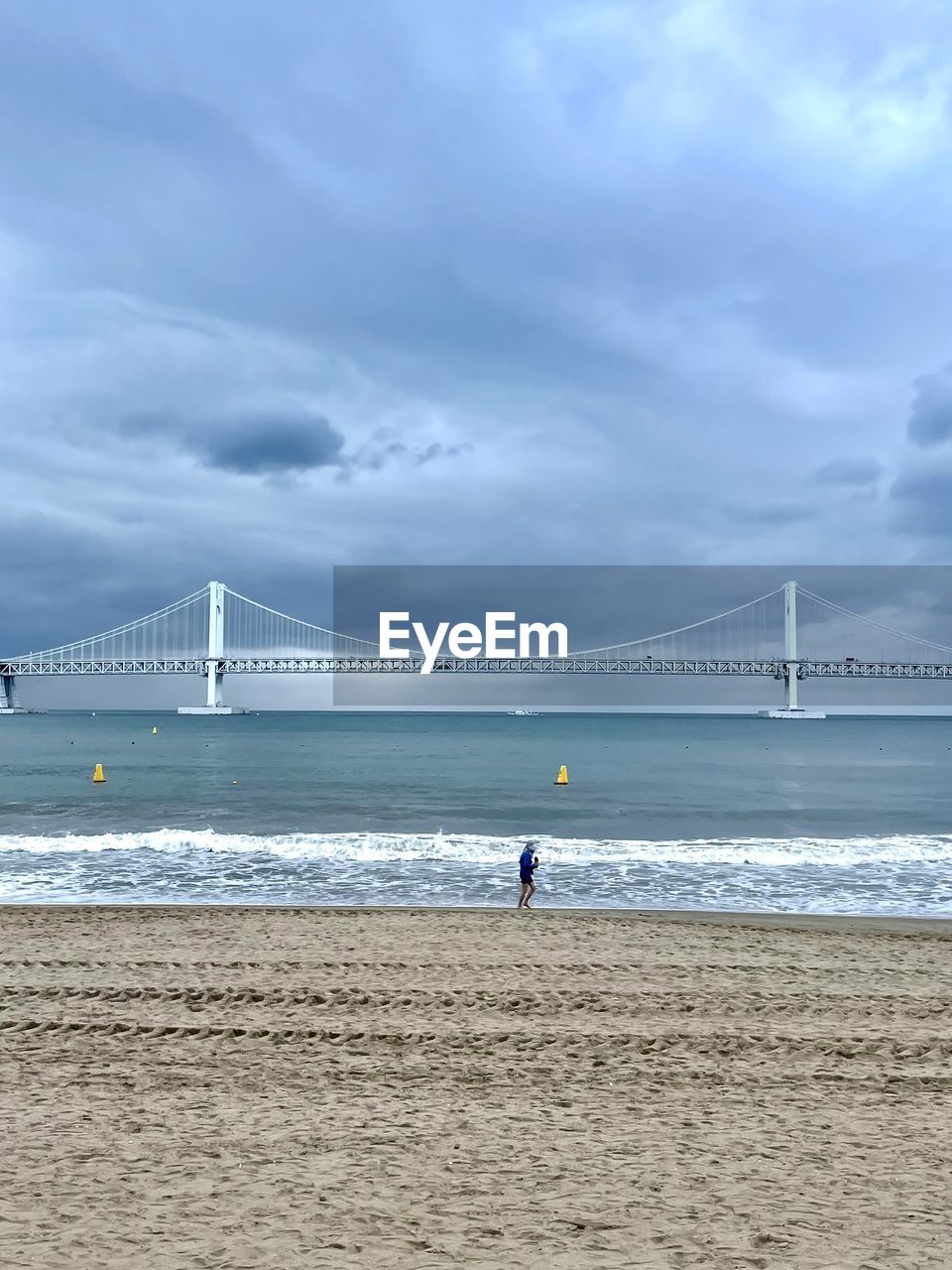 water, sea, bridge, sky, beach, built structure, architecture, suspension bridge, land, travel destinations, cloud, nature, tourism, travel, transportation, engineering, shore, horizon, sand, holiday, ocean, coast, beauty in nature, wave, scenics - nature, trip, vacation, body of water, city, pier, outdoors, day, motion, building exterior, overcast, copy space, environment, water's edge, tranquil scene, tranquility, surfing, horizon over water, bay of water, coastline, man made structure, bay, dramatic sky, landscape, sports, distant, tide