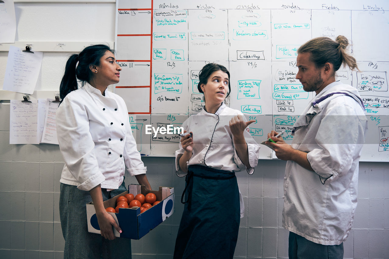 Chefs communicating against whiteboard in kitchen