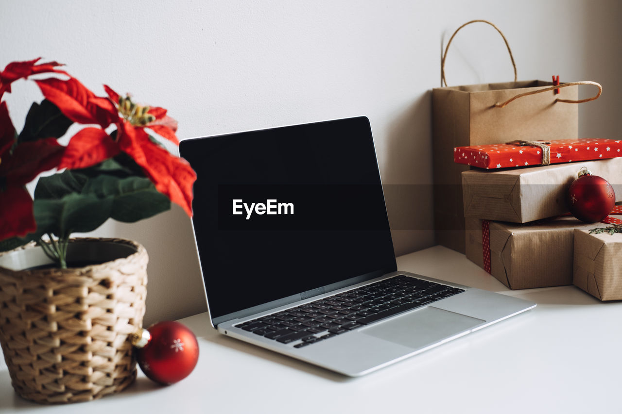 Blank display screen laptop computer with poinsettias christmas flower and gift boxes on white