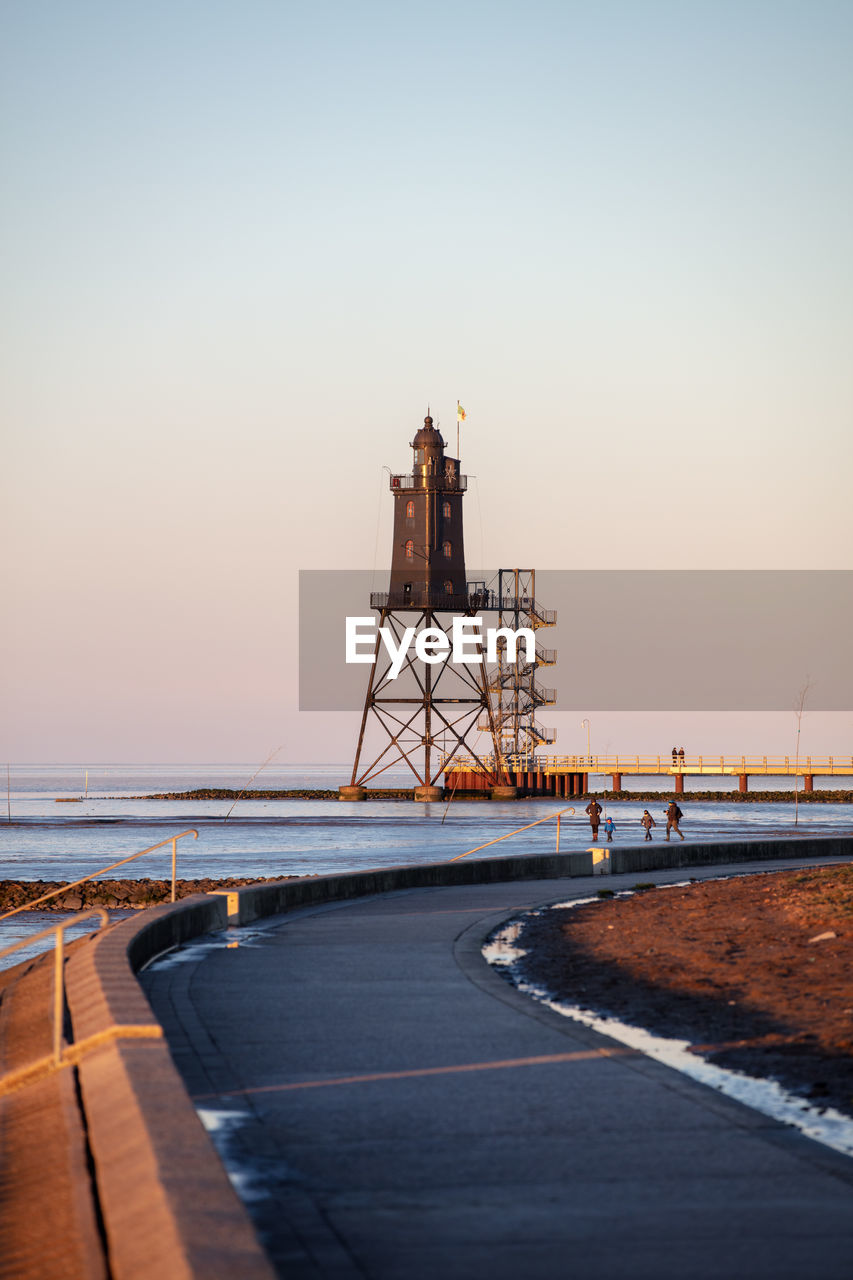 Lighthouse amidst sea against clear sky during sunset