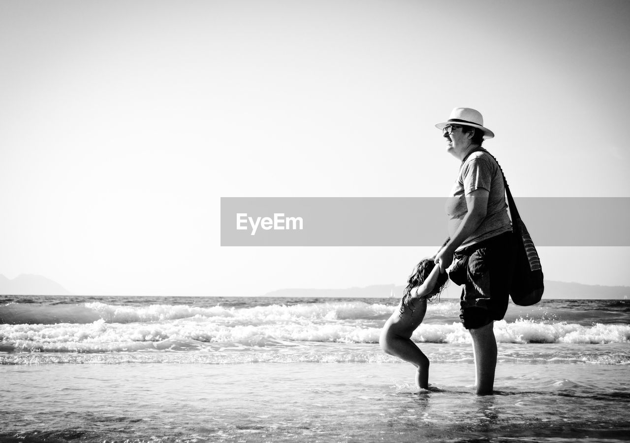 Grandmother and granddaughter standing in sea against clear sky