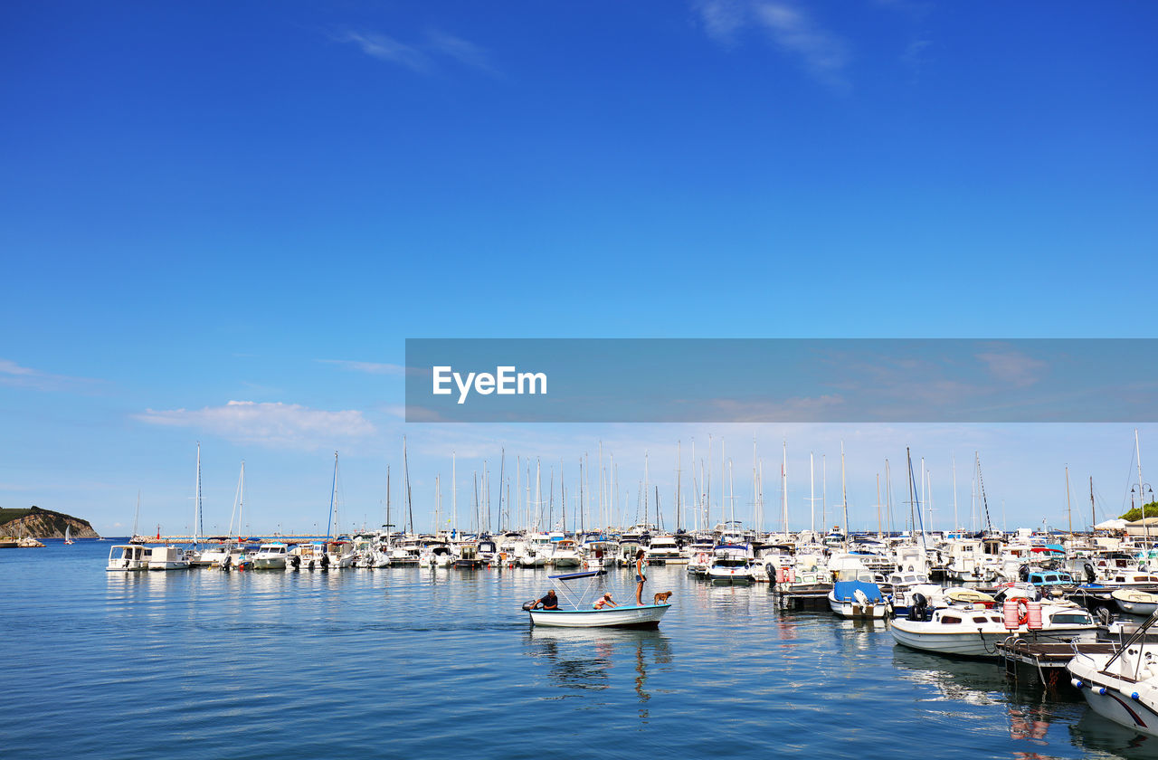Boats moored at harbor against blue sky