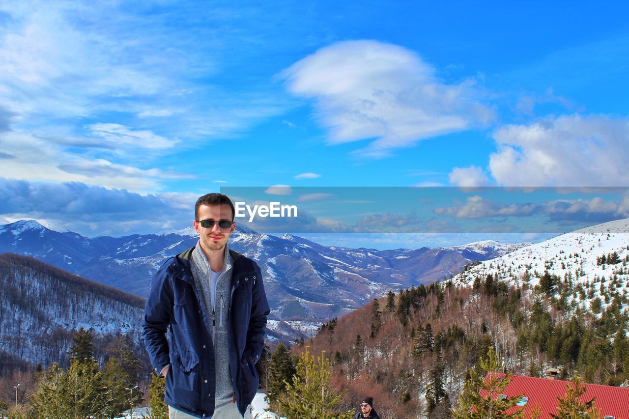 Portrait of man in sunglasses standing on snowcapped mountain