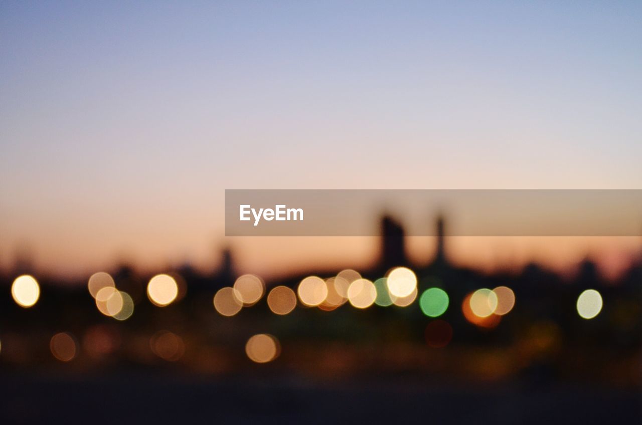 Defocused image of illuminated lights against sky during sunset