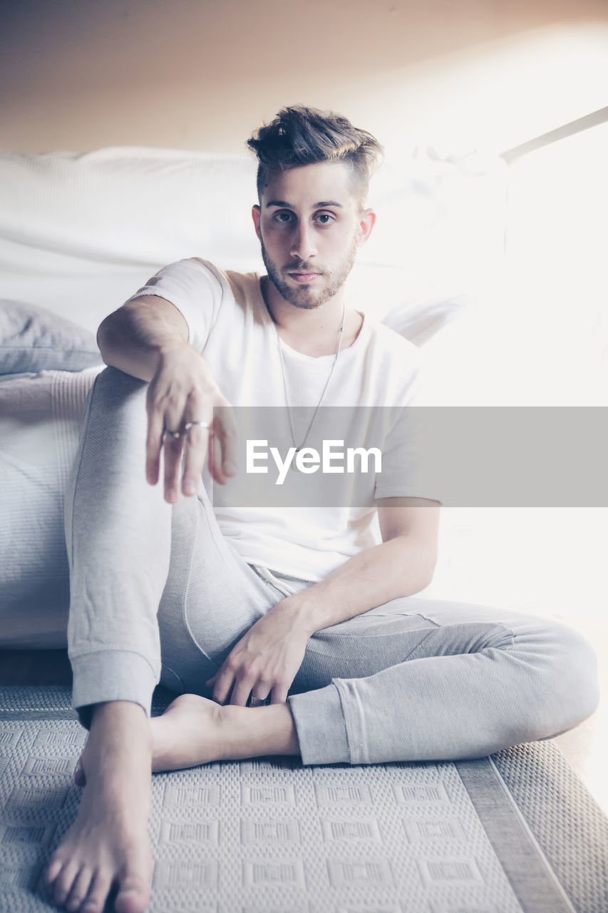 Portrait of man sitting by bed at home