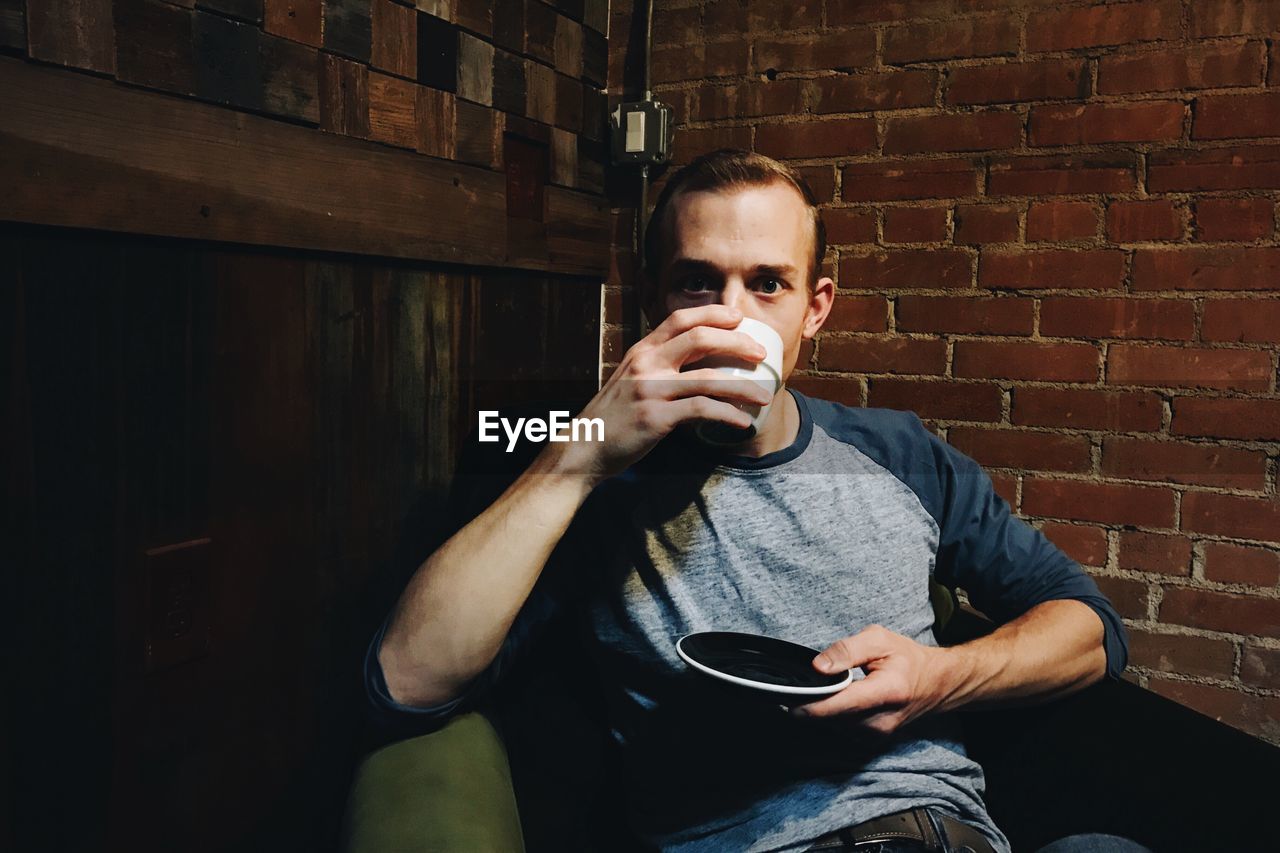 Portrait of man having drink while sitting on chair at home