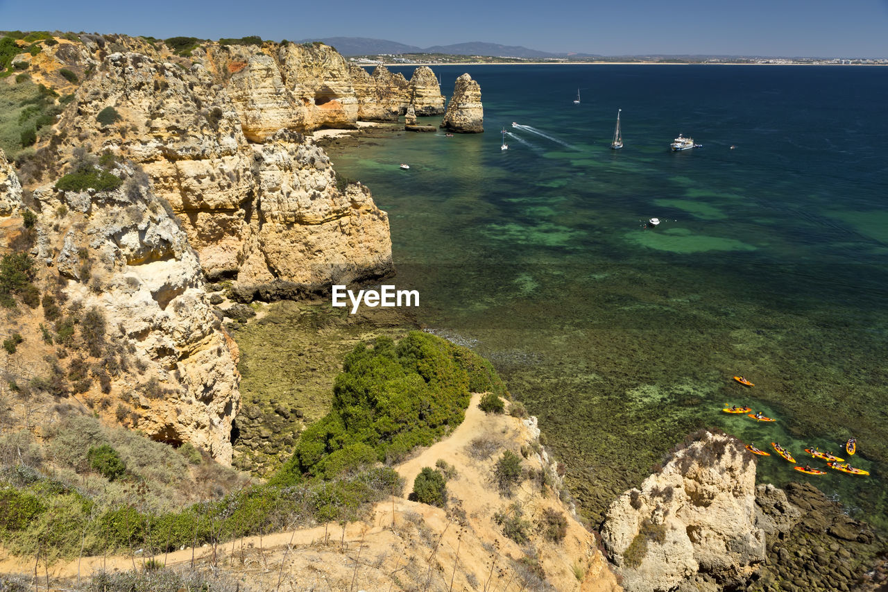 HIGH ANGLE VIEW OF ROCKS ON SEA SHORE AGAINST MOUNTAIN