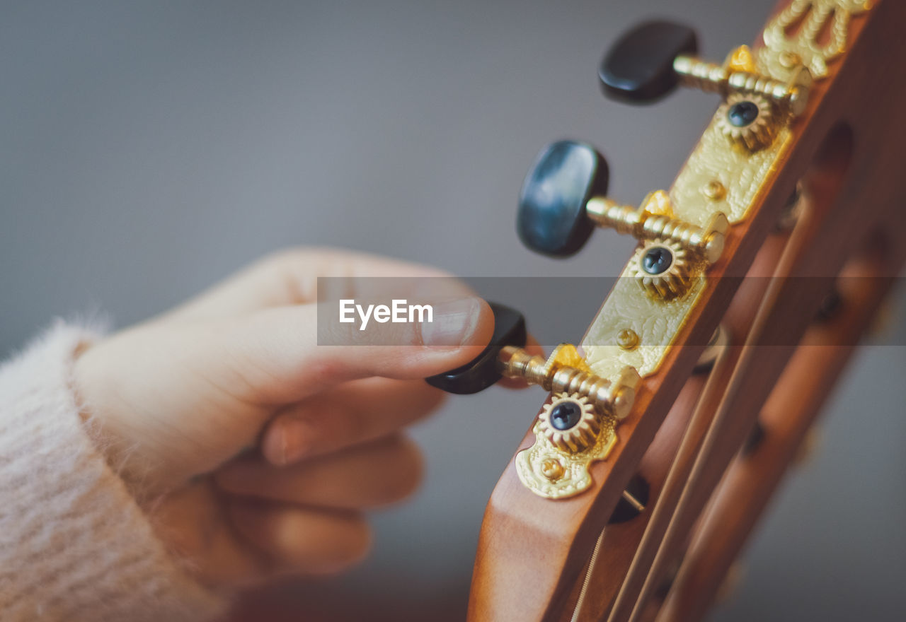 The girl twists the guitar peg while tuning the strings.