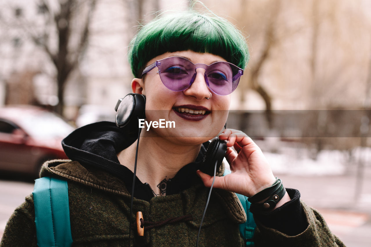 Portrait of happy non-binary hipster standing on city street