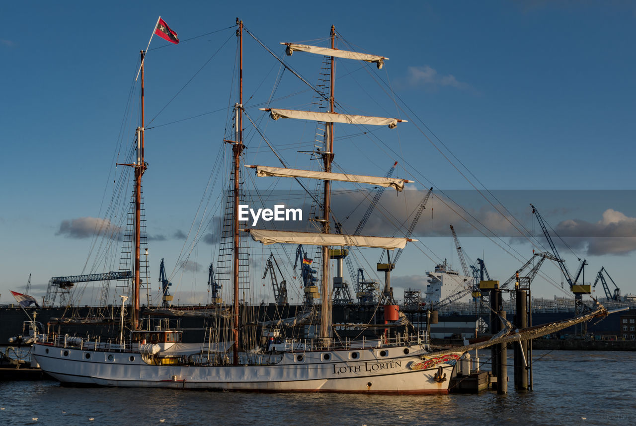 SAILBOATS MOORED IN HARBOR AGAINST SKY