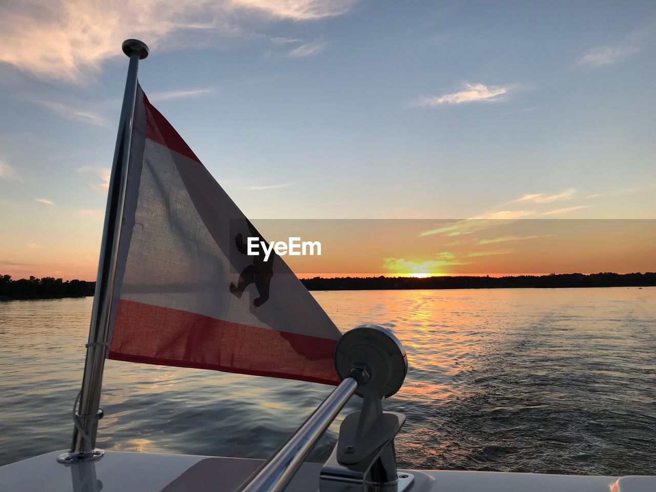 Flag on boat in sea against sky during sunset