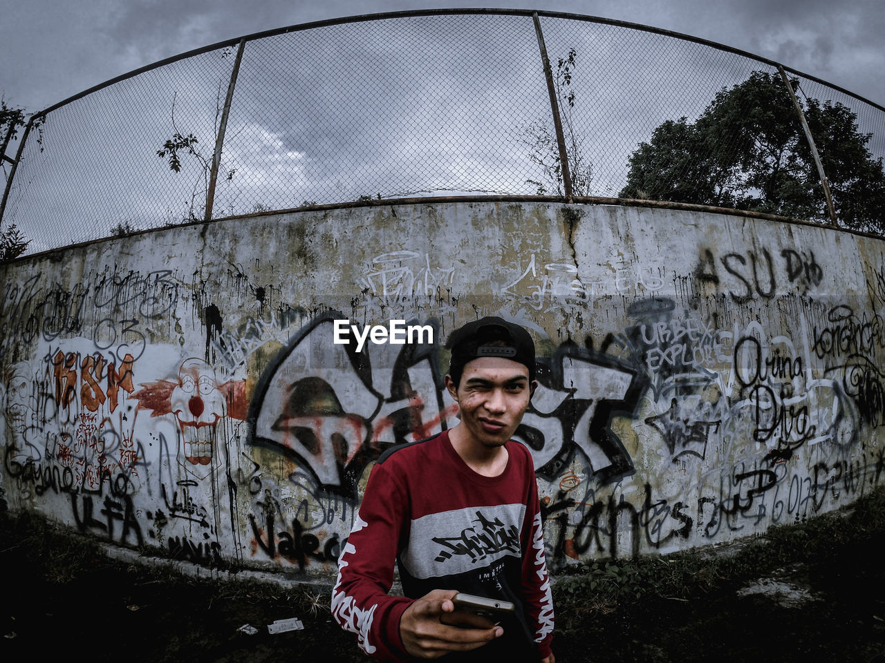 PORTRAIT OF A SMILING YOUNG MAN STANDING AGAINST GRAFFITI WALL