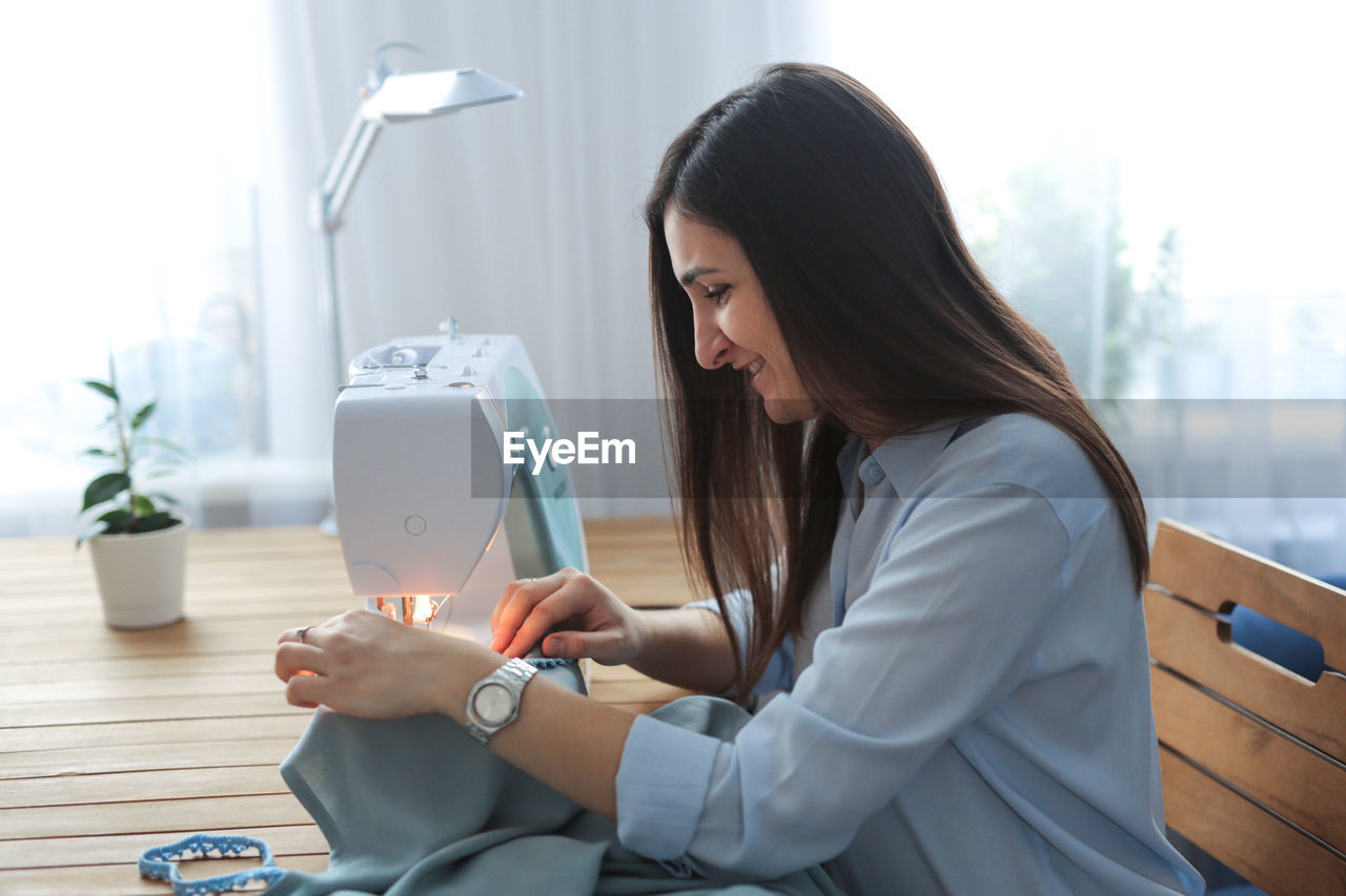Craftswoman with long black hair sews on a sewing machine in her home workshop, a real room in the 